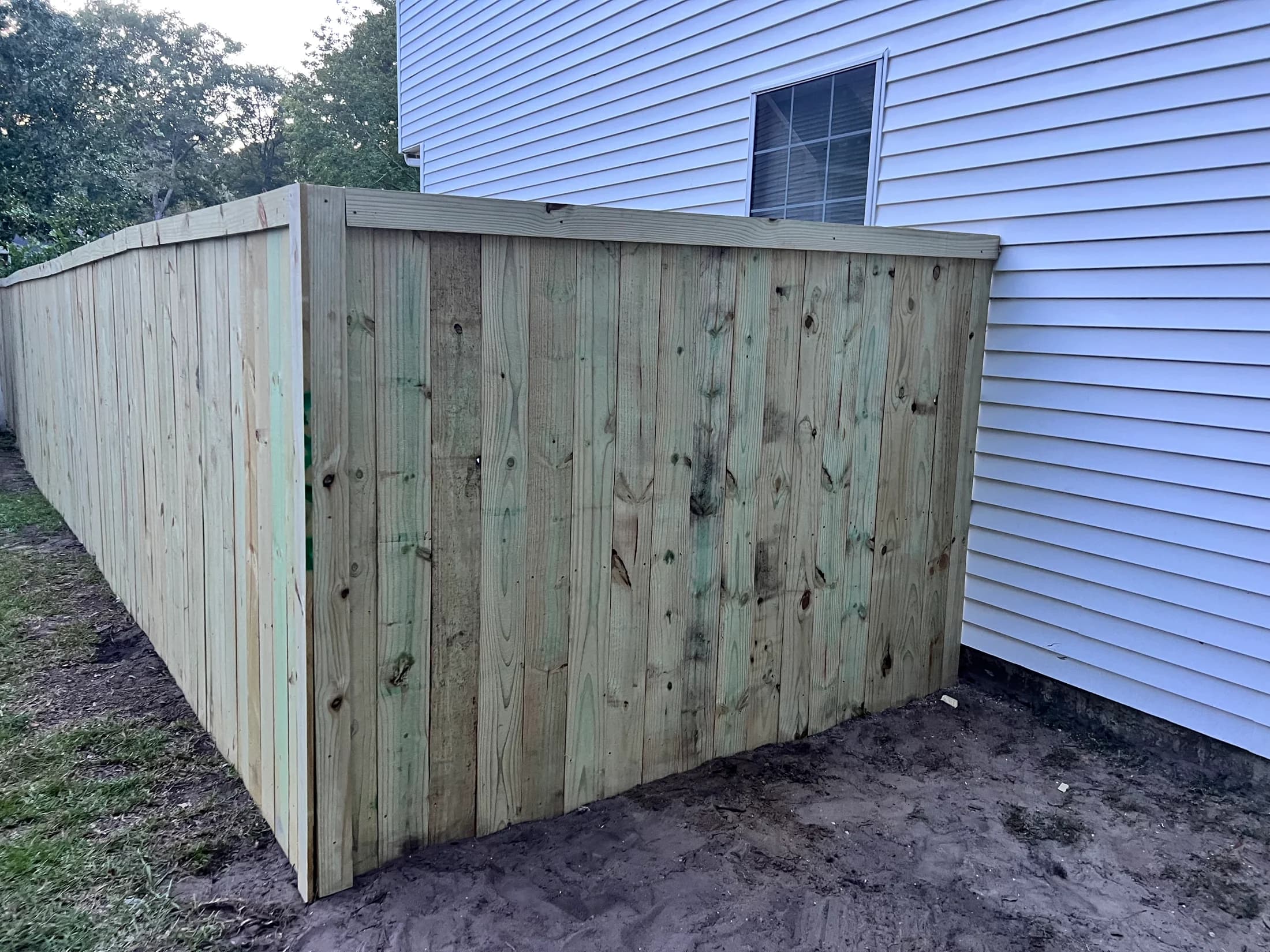 Close view of vertical fence boards, top cap, and corner post beside house siding
